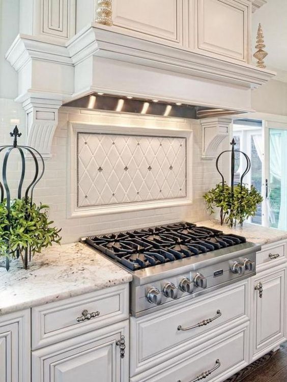 antique white kitchen cabinets with detailed embellishments are highlighted by granite countertops, a matching white range hood and a bright white tile backsplash