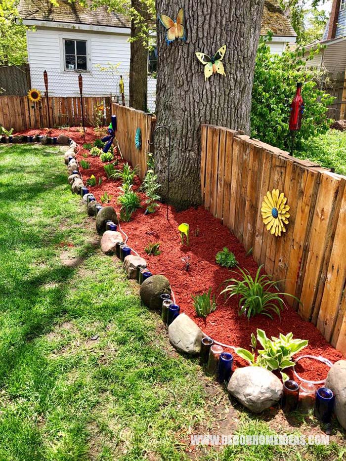 Small Garden Bed Edging Made of Rocks And Bottles. Nicely running along a wooden fence decorated with sunflowers and butterflies. #smallgarden #edging #decorhomeideas