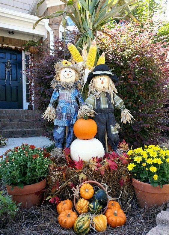 An Outdoor Fall Display Made From Scarecrows, Hay, Cornstalk, Pumpkins, Gourds, And Mums
